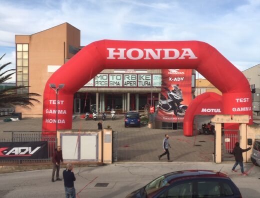 Motor Bike Di FA.DE.MA. SAS storefront with a large inflatable Honda archway, promoting motorcycle sales and service. Visible are Honda X-ADV poster, Motul signage, and parked motorbikes.