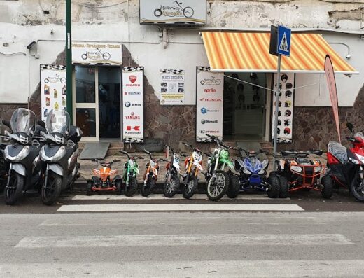 A collection of motorcycles and ATVs parked in front of Motor City Grimaldi, a motorcycle shop offering sales, service, and accessories.