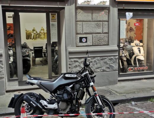 Motor Garage Napoli featuring a Husqvarna 401 motorcycle parked outside, Kymco scooter visible in the showroom window, showcasing motorcycle sales and service in Italy.