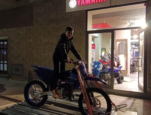 Un giovane su una moto Yamaha blu su un rimorchio di fronte a Motor Jet S.r.l., concessionario Yamaha. Servizi di trasporto moto e vendita accessori moto.