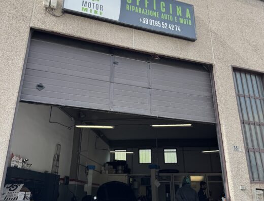 Immagine dell'officina Motor Mike, specializzata in riparazione auto e moto. L'insegna indica il numero di telefono +39 0165 52 4274. Si intravedono moto e auto all'interno dell'officina.