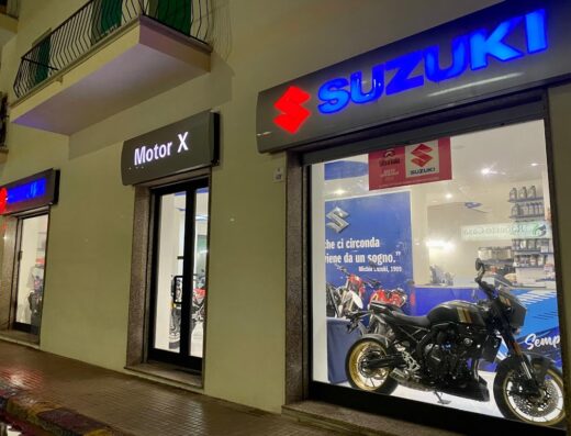 Esterno del negozio Motor X Di Delogu Alessandro con insegne Suzuki illuminate e vetrina espositiva di moto. Servizi di vendita e assistenza moto.