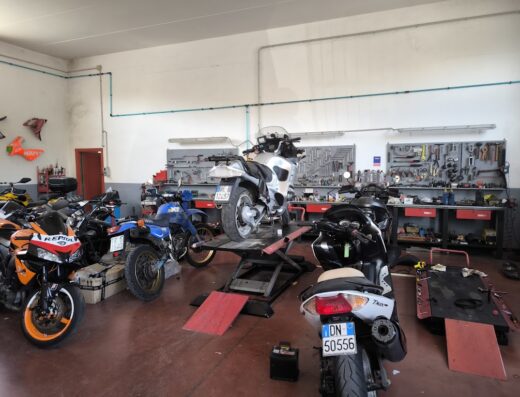Interno dell'officina Motoracing Di Menichetti Valentino, con diverse moto, tra cui una sollevata su un ponte, e attrezzature per la riparazione.