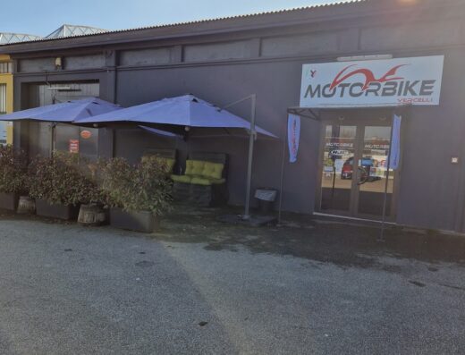 Esterno del negozio Motorbike Vercelli, con insegna ben visibile, ombrelloni esterni e sedute, che invitano i motociclisti a una sosta.