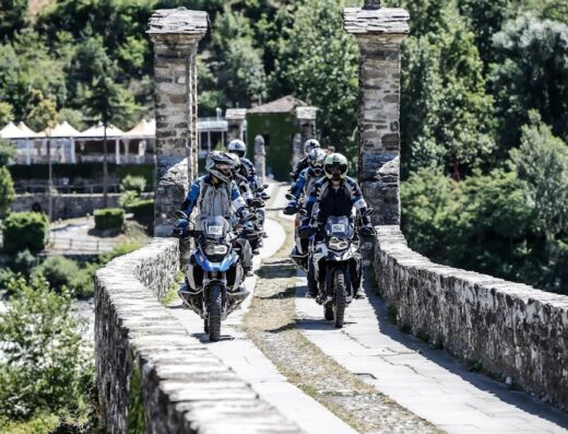 Un gruppo di motociclisti in tour su moto da enduro attraversa un ponte di pietra durante un viaggio avventura in Sardegna con MotoRentSardinia, noleggio moto e tour a Cagliari.