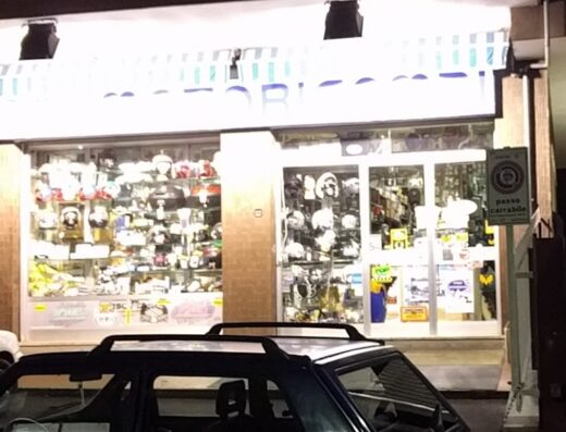 Vetrine illuminate di Motoricambi Torrevecchia, negozio di ricambi e accessori moto a Roma, con esposizione di caschi e cartello 'passo carrabile'.