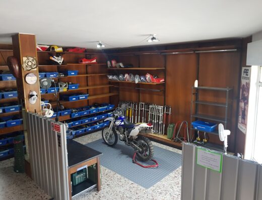 Interno di negozio di motoricambi usati: moto da cross, scaffali con ricambi, accessori moto, forcelle, sedili e attrezzature per la riparazione.