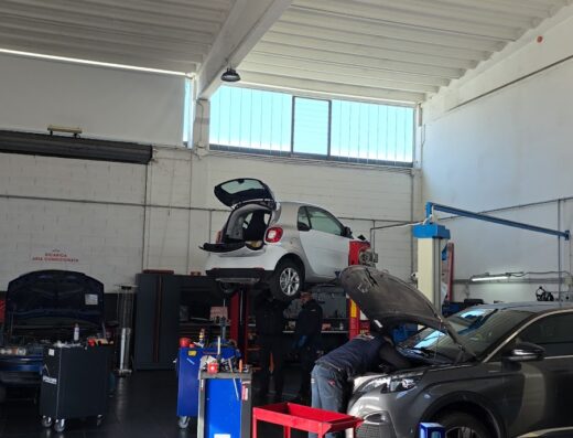 Interno di Motors Officina Meccatronica: auto su ponte sollevatore per riparazione, meccanici al lavoro su motore, attrezzature officina visibili.