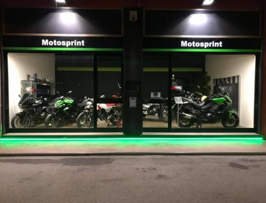 Showroom di Motosprint di Domenico Corbo con vetrina illuminata che espone diverse moto, tra cui modelli Kawasaki, in vendita.