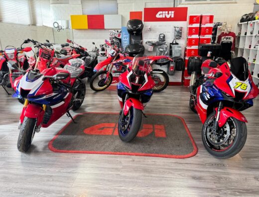 Esposizione di moto Honda rosse e blu presso la fabbrica Motostart, con accessori GIVI sullo sfondo, ideale per appassionati di motociclismo e viaggi.