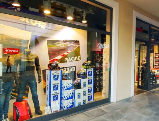 Vetrina del negozio Motostore con manichini che indossano abbigliamento da moto, caschi Shark impilati su scatole, poster di corse e accessori per motociclisti