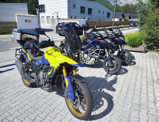 Motocicletta Suzuki giallo-blu con bauletto e due Ducati delle forze dell'ordine italiane in sosta su pavimentazione esterna.