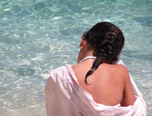 Ragazza con asciugamano rosa che guarda il mare cristallino in Sardegna, ideale per vacanze e viaggi con Motus Travel.
