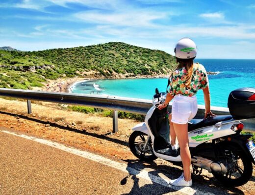 Ragazza con casco su scooter MyScoot.net a Cagliari, vista panoramica sulla spiaggia. Noleggio scooter per esplorare la Sardegna.