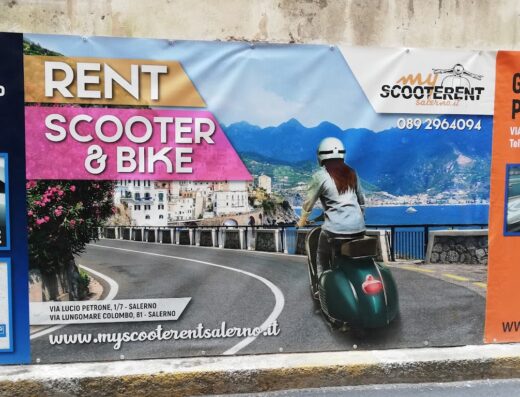 Manifesto pubblicitario di MyScooterRent&Parking24 a Salerno: noleggio scooter e bici per esplorare la Costiera Amalfitana. Donna in scooter verde con vista panoramica sul mare e la città.
