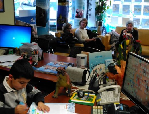 Interno dell'agenzia viaggi New Feeling Viaggi e Turismo D. A. M. di Mariano Pinna C. Sas, con un bambino che disegna e clienti in attesa.