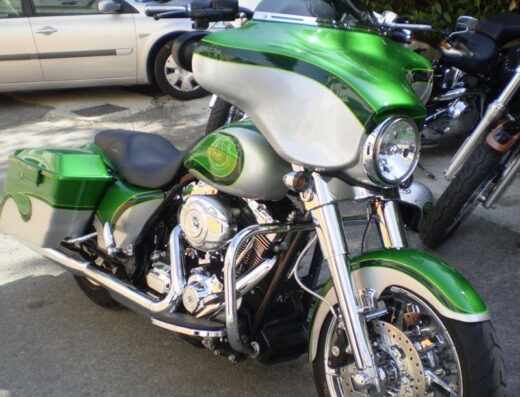 Aerografia personalizzata su moto Harley-Davidson verde e argento, dettaglio di verniciatura custom per casco e moto.