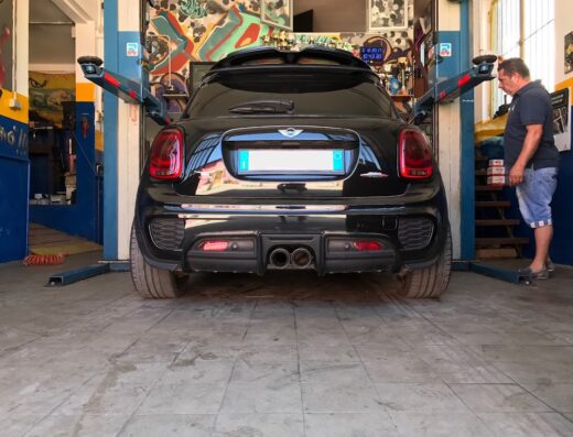 Mini Cooper nero in riparazione presso Nico Racing Service, con un meccanico che esamina il veicolo su un sollevatore idraulico.