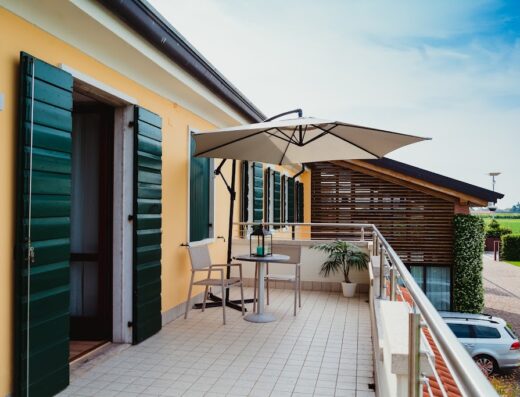 Balcone di Nido del Gelso con tavolo, sedie, ombrellone e vista sul giardino. Arredamento esterno per relax e vacanze.
