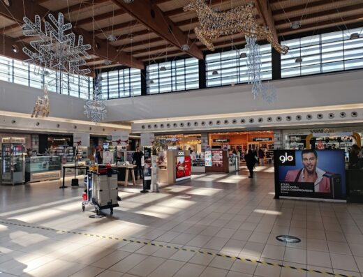 Interior view of the Adriatico shopping center, featuring various retail stores, holiday decorations hanging from the ceiling, and tiled flooring.