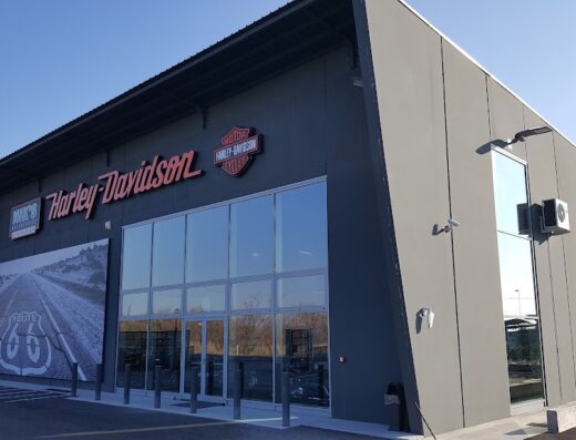 Showroom Nik's Harley-Davidson con insegne del marchio, vetrine ampie che mostrano moto, e un'immagine della Route 66. Servizi di vendita e assistenza Harley-Davidson.