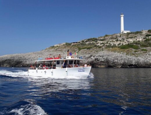 Immagine di una barca bianca con passeggeri che naviga vicino alla costa di Nettuno, con un faro sullo sfondo.