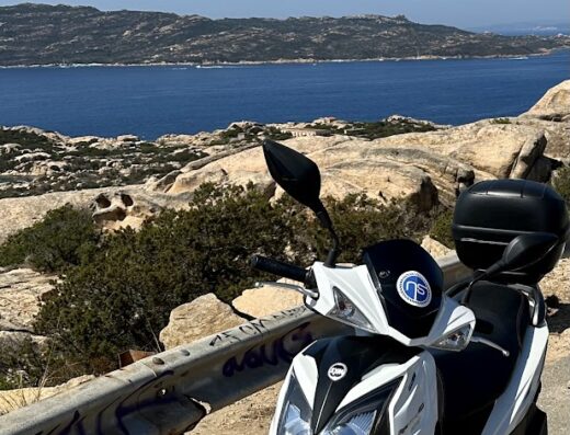 Noleggio scooter a La Maddalena, Sardegna. Vista panoramica con moto bianca parcheggiata, ideale per esplorare l'arcipelago in libertà. Servizio di rent bike & moto per un'esperienza indimenticabile.