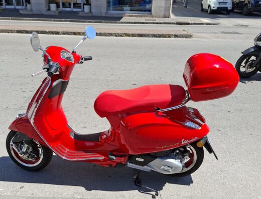 Noleggio scooter a Salerno: Vespa rossa parcheggiata in strada con bauletto, ideale per esplorare la città con Futura Rent.