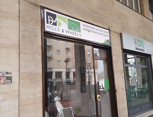 Vetrine di negozio di noleggio moto, auto e furgoni, con scooter bianco in esposizione. Servizi di noleggio per viaggi e turismo.