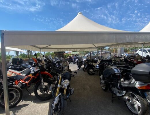 Parcheggio di moto di diverse marche e modelli sotto un tendone bianco con cielo azzurro sullo sfondo, evento motociclistico Non Solo Boxer.