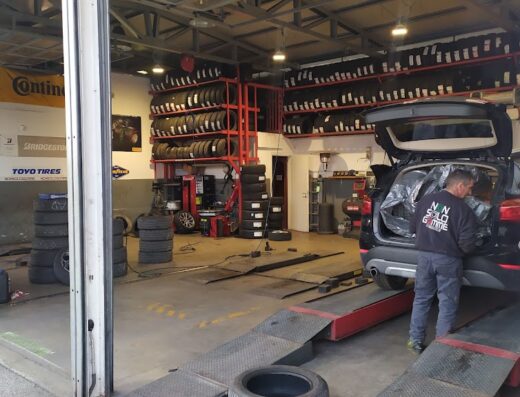 Interno dell'officina Nonsologomme S.A.S. con scaffali di pneumatici, auto in riparazione e operatore al lavoro. Servizi di montaggio e vendita pneumatici.