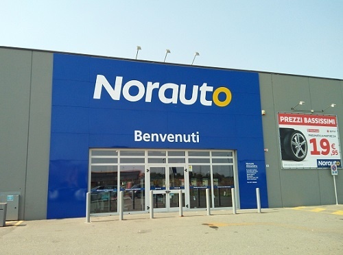 Norauto Alessandria: ingresso del negozio di accessori e ricambi auto con insegna "Benvenuti" e offerta pneumatici a prezzi bassissimi.