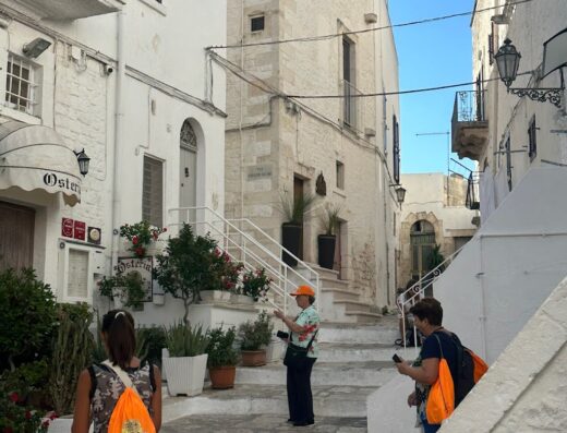 Turisti in una pittoresca via di Ostuni, Puglia, con edifici imbiancati a calce, scalinata e vegetazione. Servizi di viaggio Oasisardinia.