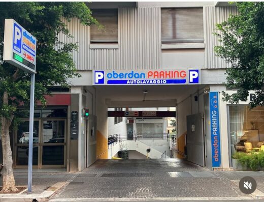 Ingresso del parcheggio Oberdan con segnaletica luminosa, servizio di autolavaggio, e indicatore di posti liberi, ideale per motociclisti e automobilisti in viaggio.