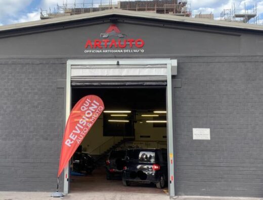 Officina Artigiana dell'Auto: facciata dell'officina che offre servizi di revisione auto e moto, con auto all'interno e bandiera promozionale.