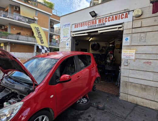 Officina Auto-Moto Alessio: A red car with its hood open is parked outside the garage, where a motorcycle repair is in progress. Autofficina Meccanica is visible above the garage entrance.