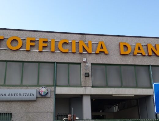Facciata dell'Autofficina Danilo, officina autorizzata Lancia e Alfa Romeo, con insegna gialla e cartello di parcheggio. Servizi di riparazione moto e auto.