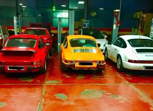 Garage interior featuring a collection of classic Porsche 911s in various colors, showcasing automotive service and restoration expertise at Officina Ferrato.