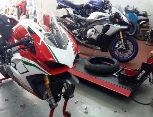 Moto Ducati Panigale V4 in officina Moto Racing Point Acilia, con moto Yamaha sullo sfondo e attrezzatura per riparazione pneumatici, servizio di assistenza moto e riparazione