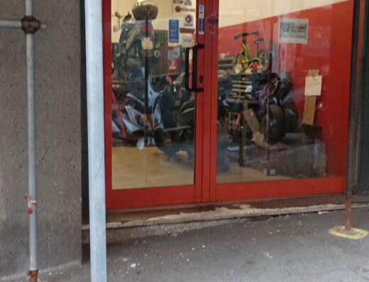 Officina moto e scooter a Genova: vetrina con moto e scooter in riparazione, cartello passo carrabile e impalcatura esterna.