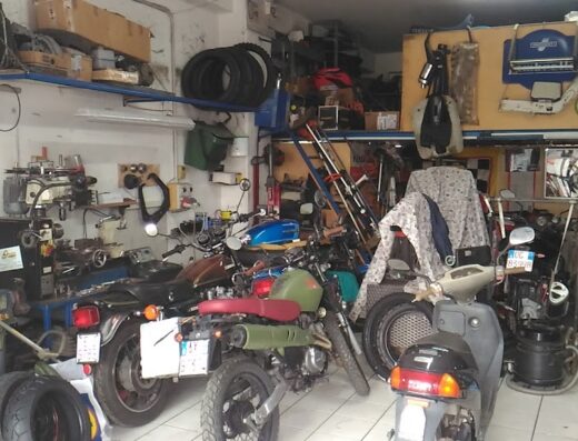 Interno dell'officina moto di Marco Pasquale, con diverse motociclette in riparazione, scaffali con ricambi e attrezzature per la manutenzione e la riparazione di moto.