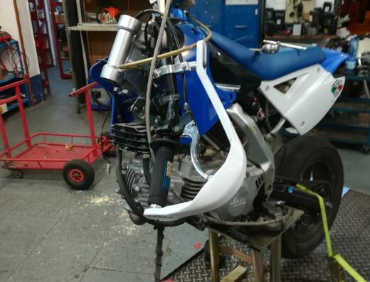 Officina motocicli F.lli Romeo: Motocicletta da corsa blu e bianca in riparazione su cavalletto, con parti smontate e attrezzi visibili, in officina.