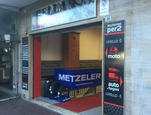 Ingresso dell'officina Bella Gomme a Sanremo, specializzata in pneumatici Metzeler per moto e auto, con cartello indicante i livelli di servizio.