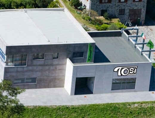 Officina Tosi Moto: vista esterna dell'edificio che ospita l'officina di riparazione e personalizzazione moto, con logo ben visibile e bandiere decorative.