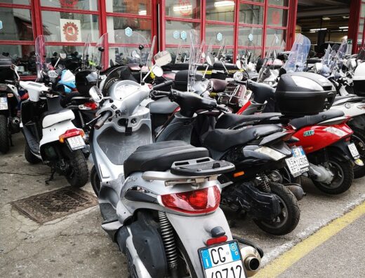 Officina Vespa: Scooter parcheggiati di fronte all'officina Gilera, con vetrate rosse. Dettaglio dello scooter argento in primo piano.
