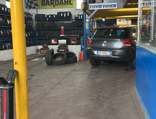 Interno dell'officina Cavallo con auto in riparazione, scaffali di pneumatici e cartelli Bardahl e Toyo Tires. Servizi di riparazione e manutenzione auto.