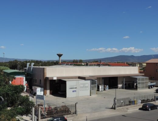 Officine Ferrocar building exterior, featuring its service bays, signage and surrounding landscape under a clear blue sky.