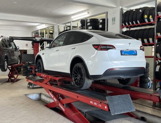 Auto bianca su ponte sollevatore per riparazioni presso Officine Imperiesi, con scaffali di pneumatici sullo sfondo.