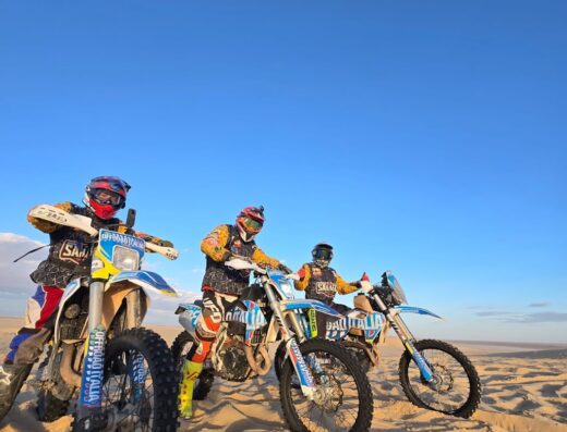 Tre motociclisti di Offroad Italia con moto da enduro nel deserto, abbigliamento tecnico e caschi, pronti per l'avventura e il viaggio offroad.