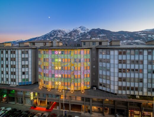 Vista esterna dell'Omama Social Hotel, hotel moderno e colorato con montagne innevate sullo sfondo, situato ad Aosta.